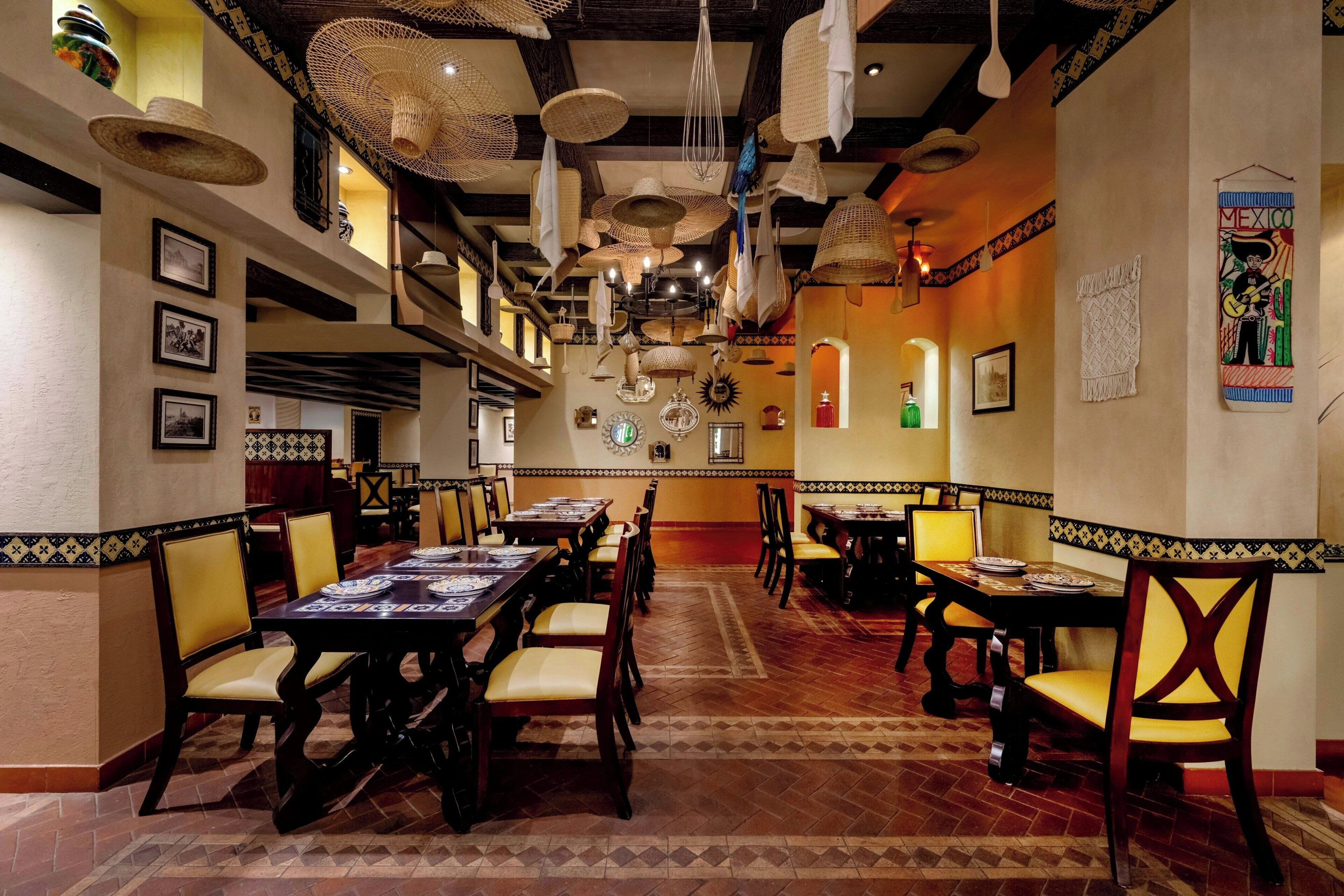 A restaurant with multiple dining tables and chairs, a patterned floor, and hanging decorative items.