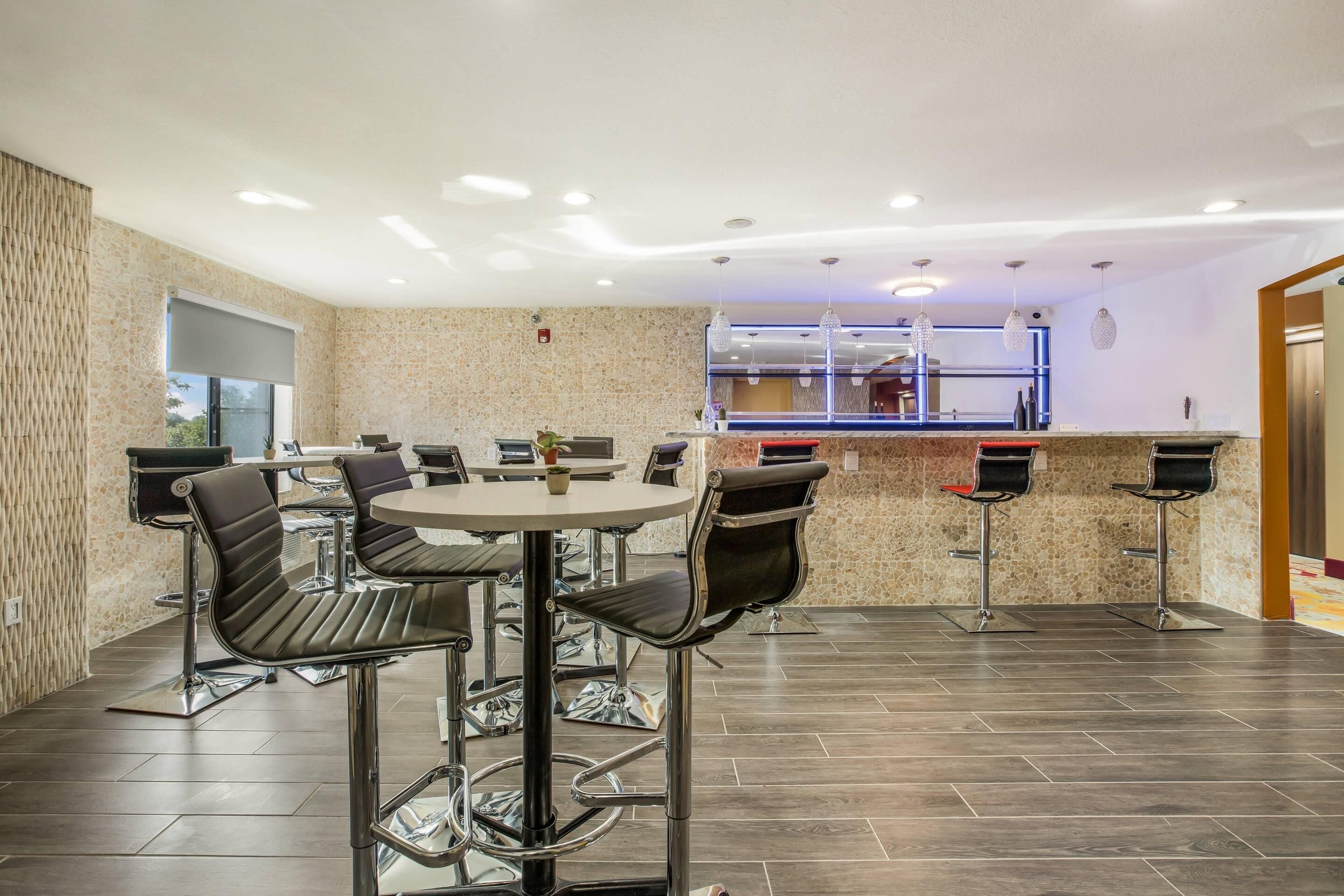 A modern bar area with a round table and bar stools, a counter with a blue backlit display, and a stone-textured wall.