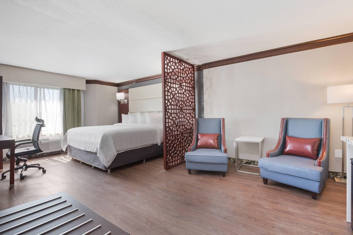 A hotel room with a bed, two armchairs, a desk, and a chair.