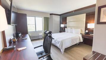 A hotel room with a bed, desk, chair, TV, and a window with curtains.
