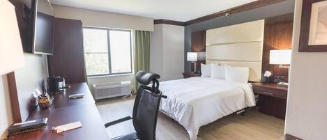 A hotel room with a bed, desk, chair, TV, and a window with curtains.