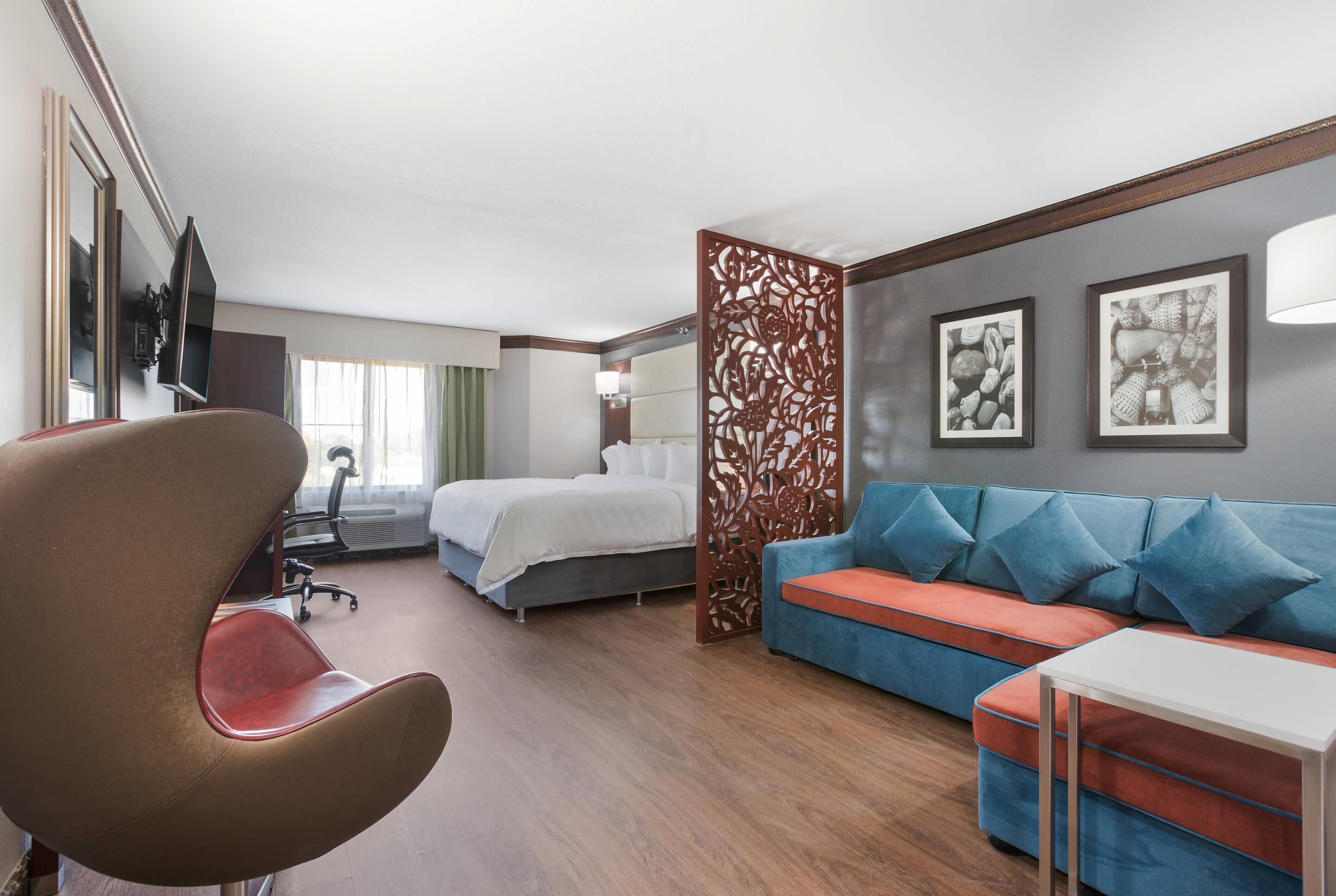 A hotel room with a bed, a sofa, a desk, a chair, and a decorative partition.