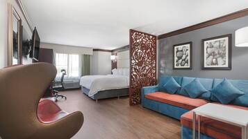 A hotel room with a bed, a sofa, a desk, a chair, and a decorative partition.