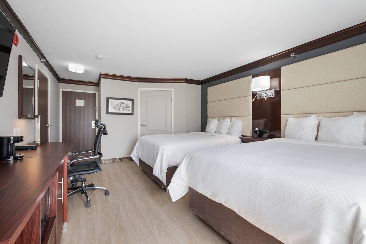 Habitación de hotel con dos camas, un escritorio, una silla y un espejo grande.