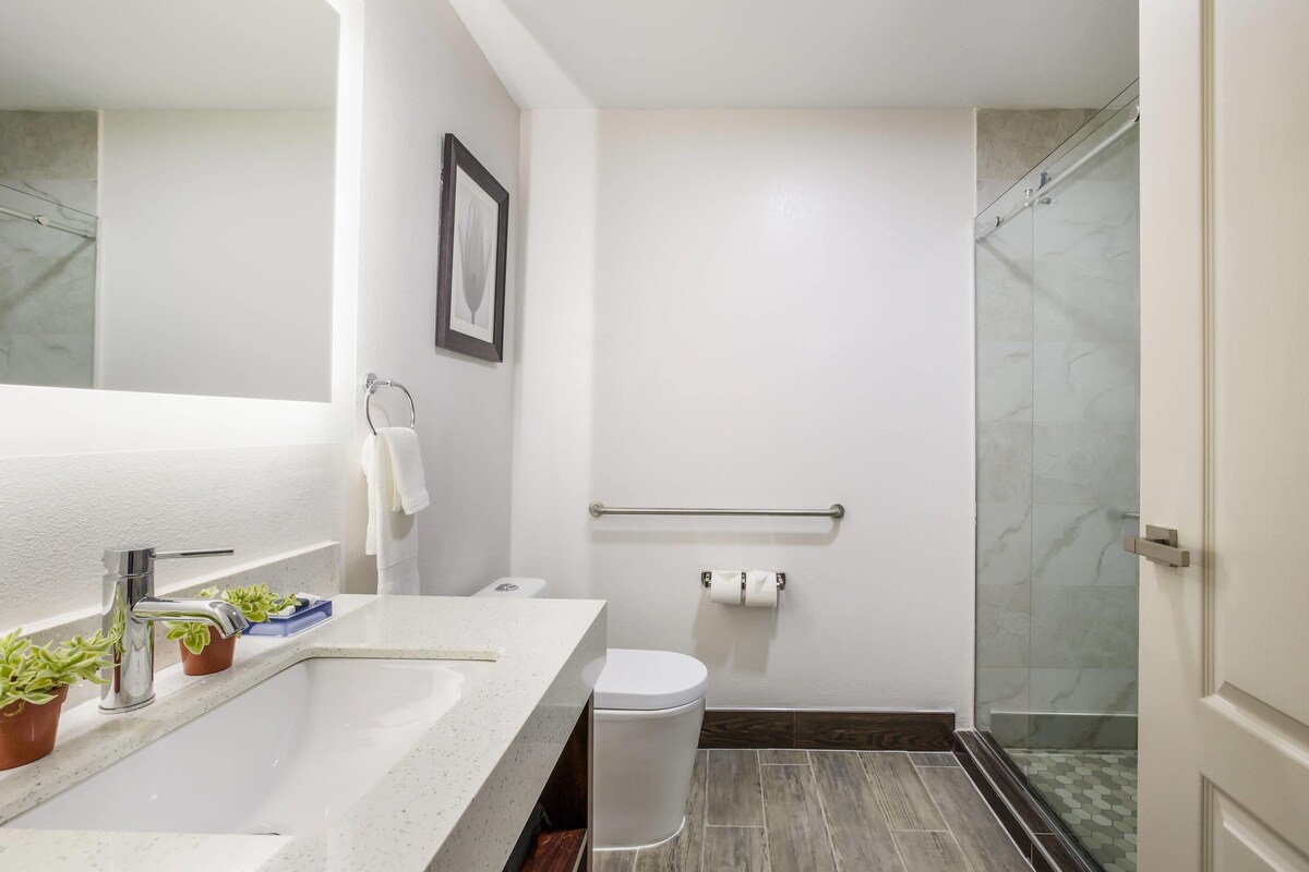 Un baño moderno con un lavabo blanco, un inodoro, una ducha con puertas de vidrio y un cuadro enmarcado en la pared.