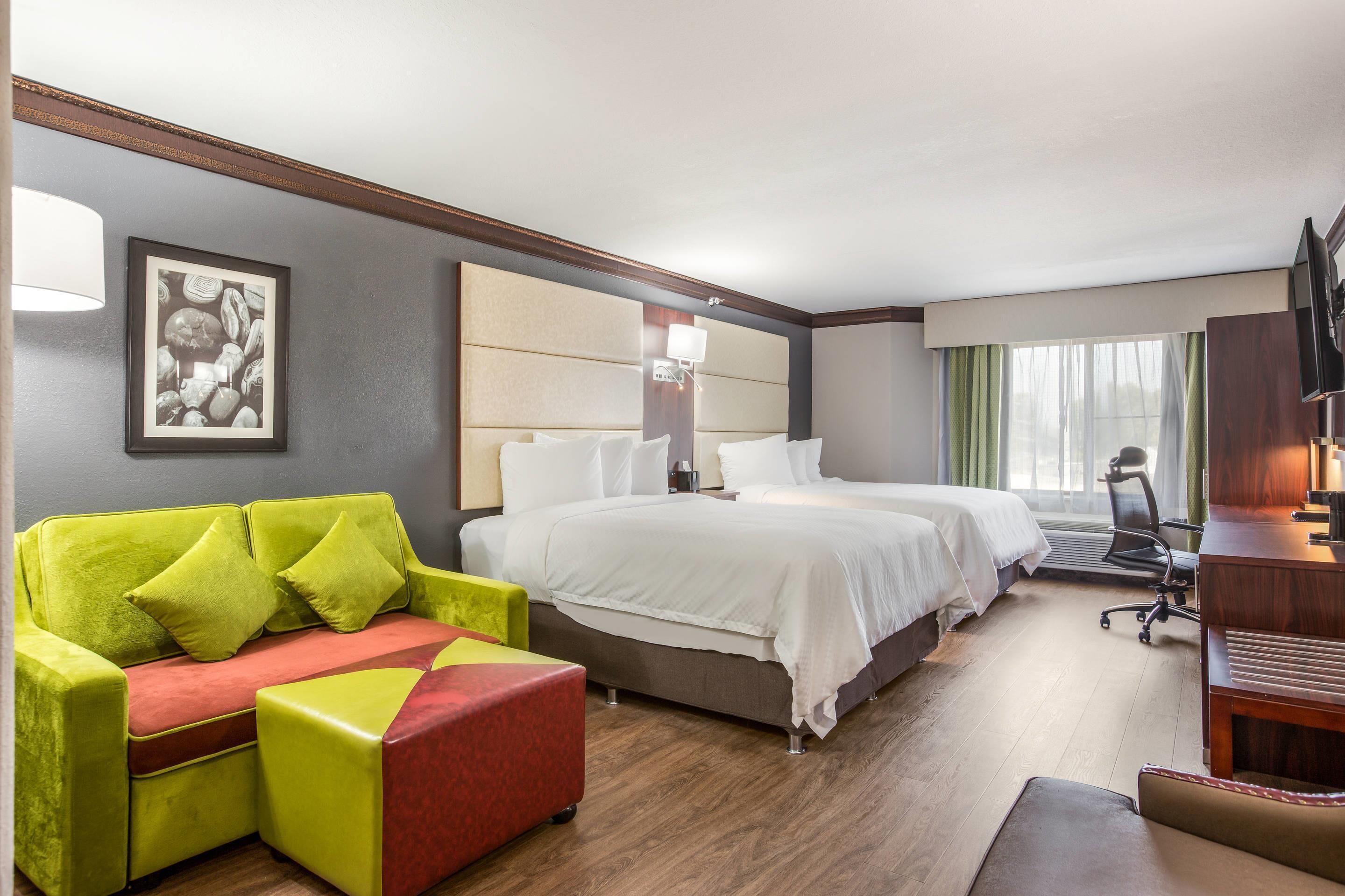 A hotel room with two beds, a sofa, a desk, and a TV.
