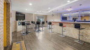 Un espace bar moderne, doté de nombreux tabourets, d’un comptoir et d’un grand écran de télévision.
