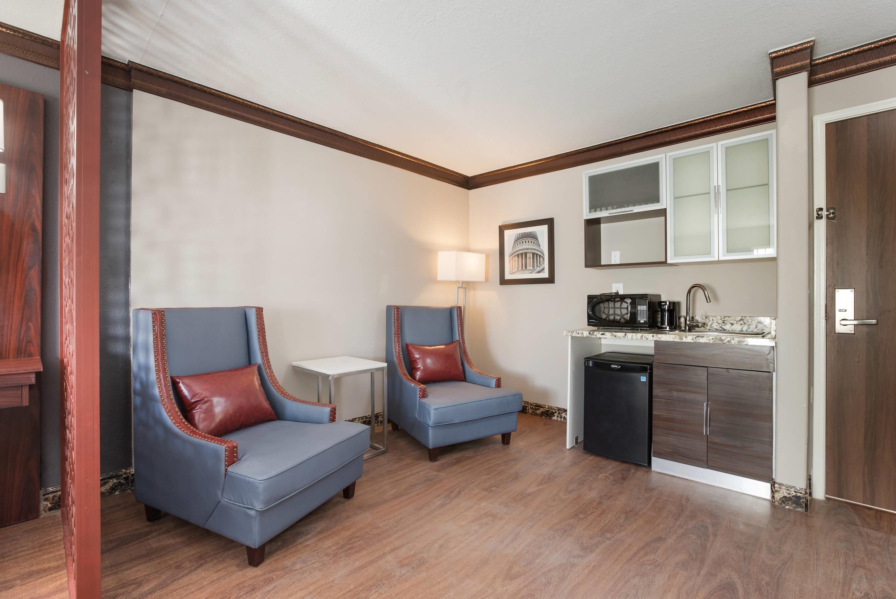 Una habitación compacta con dos sillones azules, una mesita, una lámpara y una zona de cocina con microondas y lavavajillas.