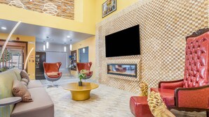 A modern living room with a sofa, red chairs, a round coffee table, and a mounted TV. - The Leo Collection Detroit, an Ascend Collection Hotel (Lincoln Park)