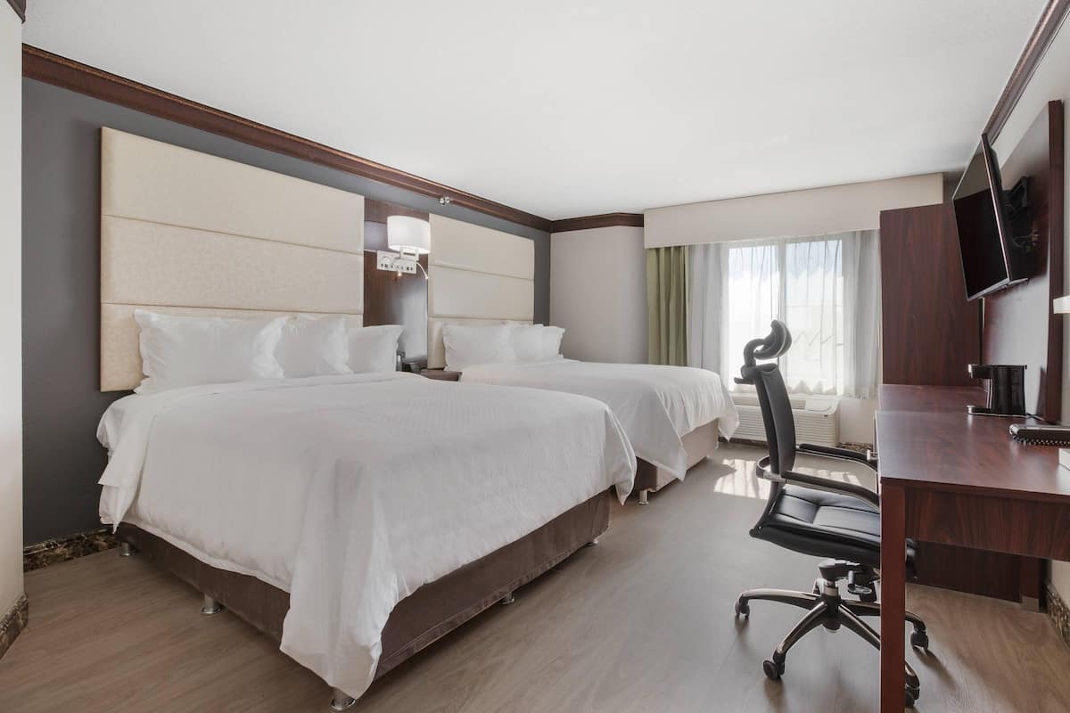 A hotel room with two beds, a desk, a chair, a TV, and a window with curtains.