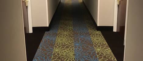 Un pasillo de hotel con alfombra estampada, paredes blancas y puertas a ambos lados.
