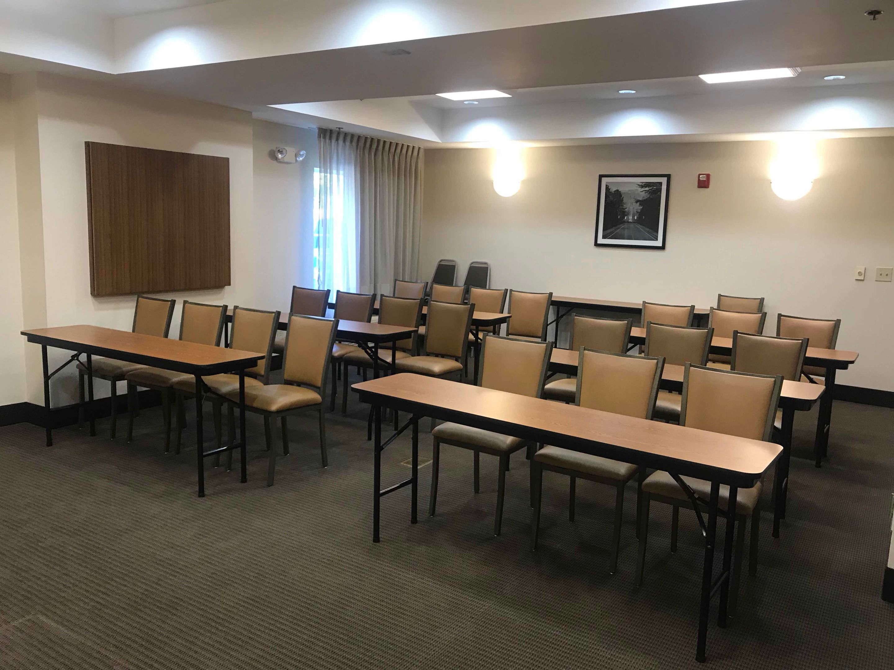 Une salle de conférence avec plusieurs tables et chaises, un panneau en bois au mur et un tableau encadré.