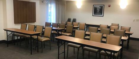Une salle de conférence avec plusieurs tables et chaises, un panneau en bois au mur et un tableau encadré.
