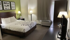 A hotel room with a bed, bedside lamps, a desk with a computer, an air conditioner, and framed pictures on the wall. - Sleep Inn Raleigh Durham Airport (Durham)