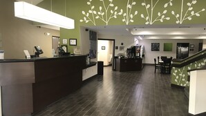 A reception area with a dark wood reception desk, a green wall with white leaf patterns, and a tiled floor. - Sleep Inn Raleigh Durham Airport (Durham)