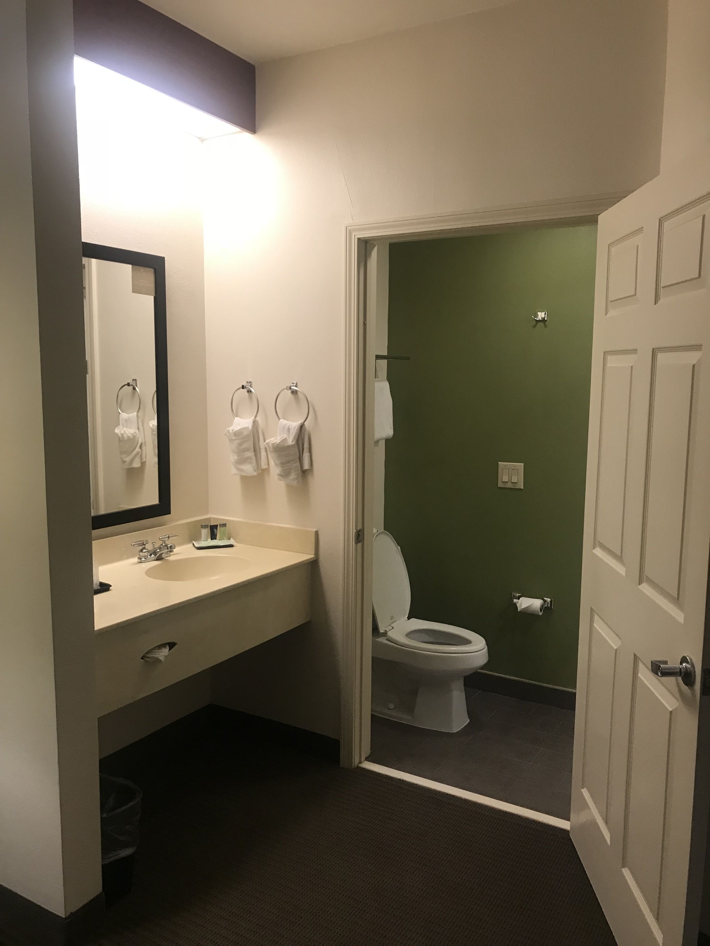 A bathroom with a sink, mirror, towel rings, and a toilet.