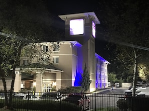 A building with a prominent clock tower, a gated entrance, and a parking area with several cars.