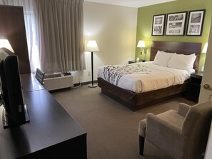A hotel room with a bed, bedside lamps, a desk with a computer, a chair, and a window with curtains.