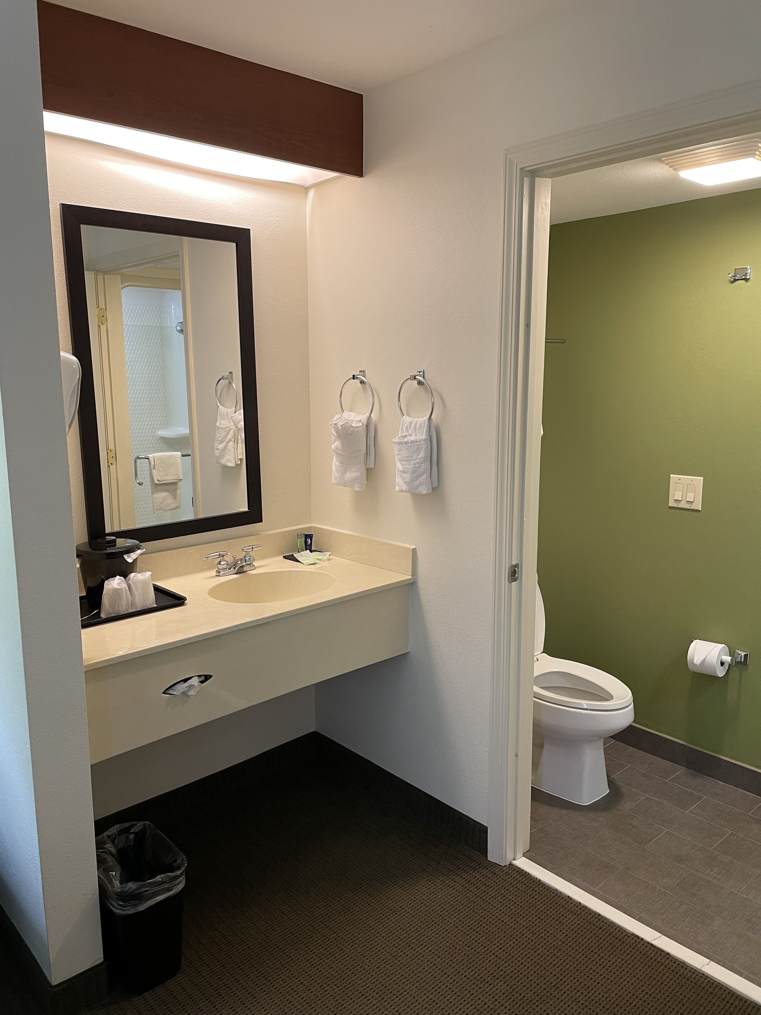 Un baño con lavamanos, espejo, toallero y retrete.