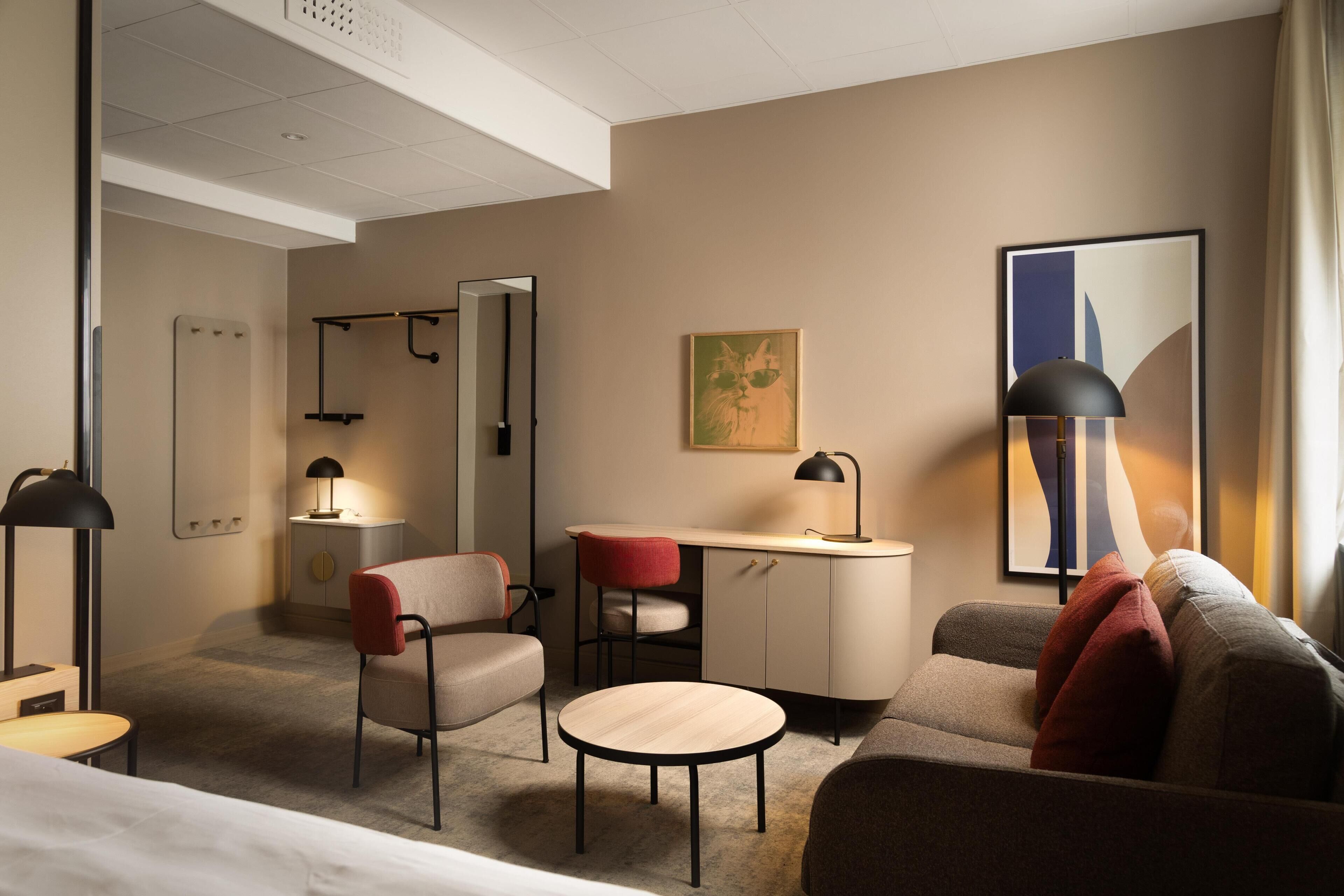 Habitación de hotel con cama, escritorio, silla, sofá, mesa redonda y espejo.