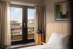 A hotel room with a bed, a nightstand, a lamp, and a window with curtains.