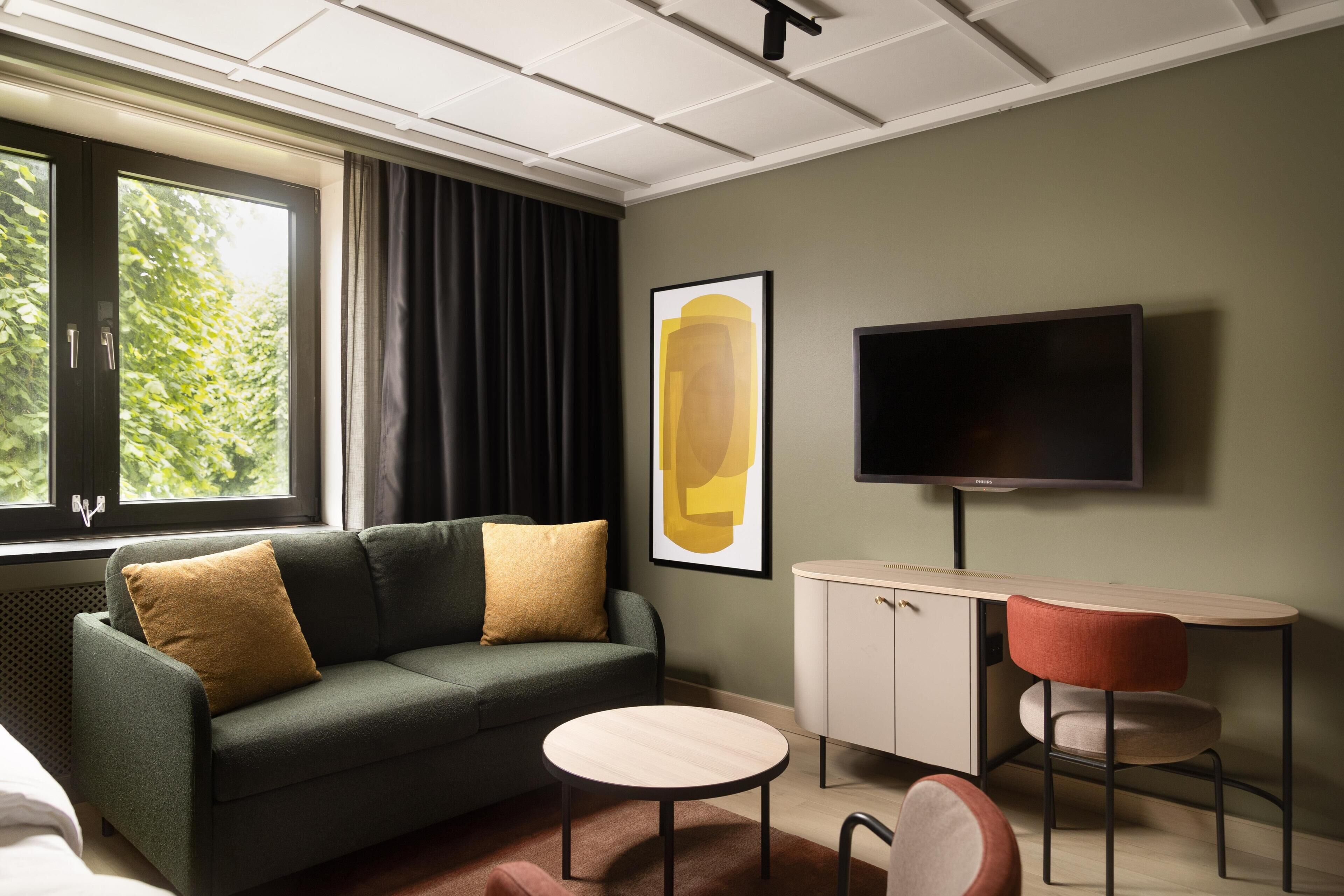 A modern hotel room with a sofa, a small round table, a TV, and a cabinet.