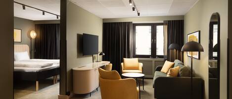 A hotel room with a bed, a desk, a sofa, a chair, a TV, and a large window.