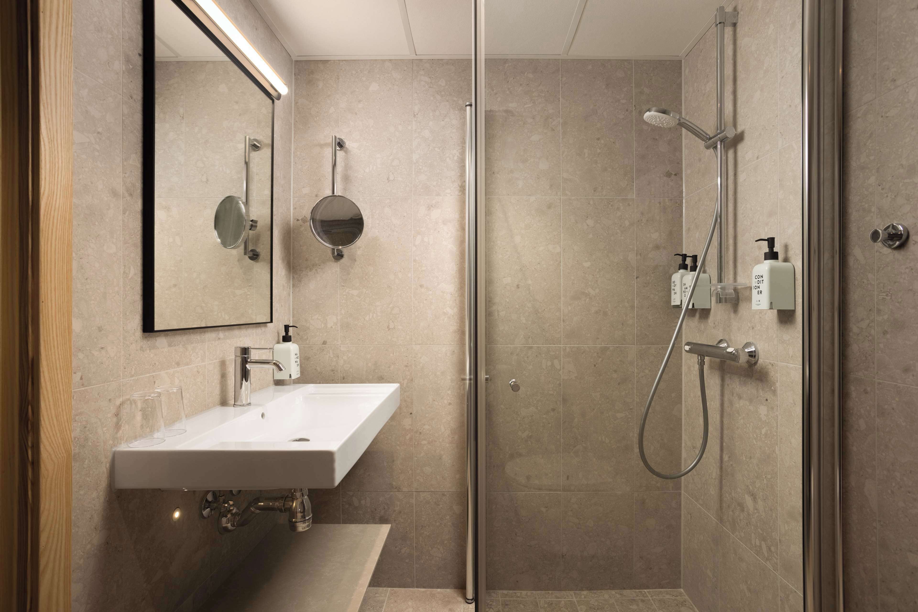 A modern bathroom with a glass shower enclosure, a white sink, and a mirror.