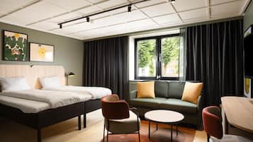 Habitación de hotel con cama, dos sillones, sofá, mesita y ventana con cortinas.
