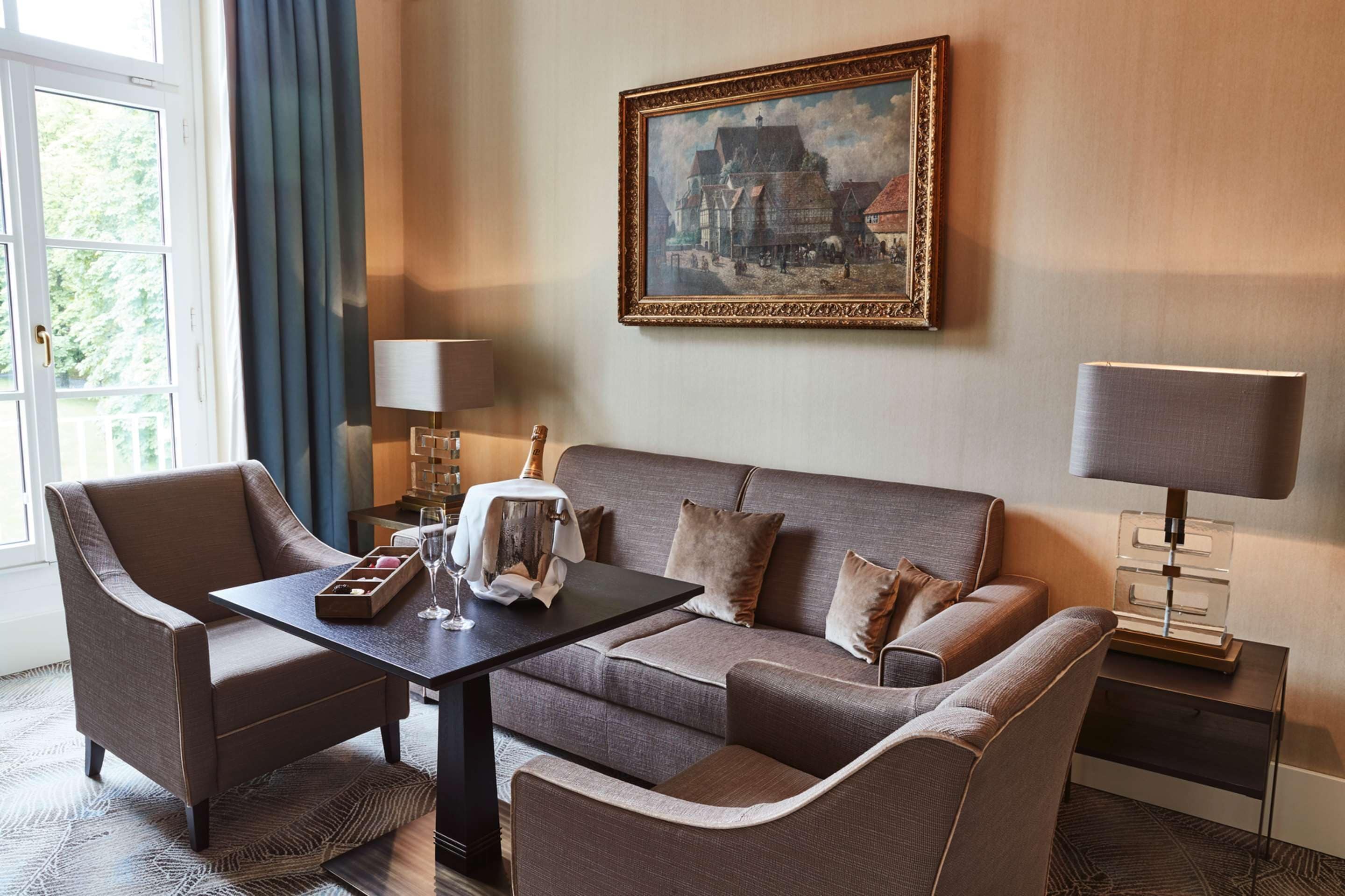 A hotel room with a sofa, armchairs, a coffee table, a painting, and a lamp.
