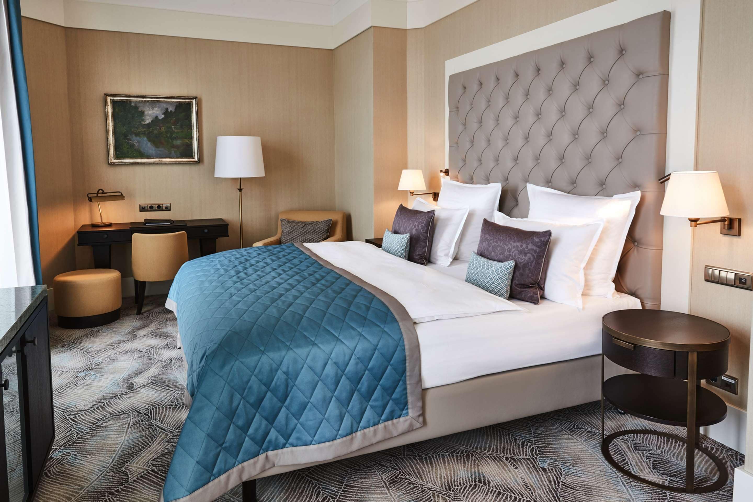 A hotel room with a large bed, two bedside tables, a desk, a chair, and a painting on the wall.