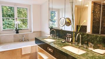 A modern bathroom with two sinks, a large mirror, and a window with a view of greenery.
