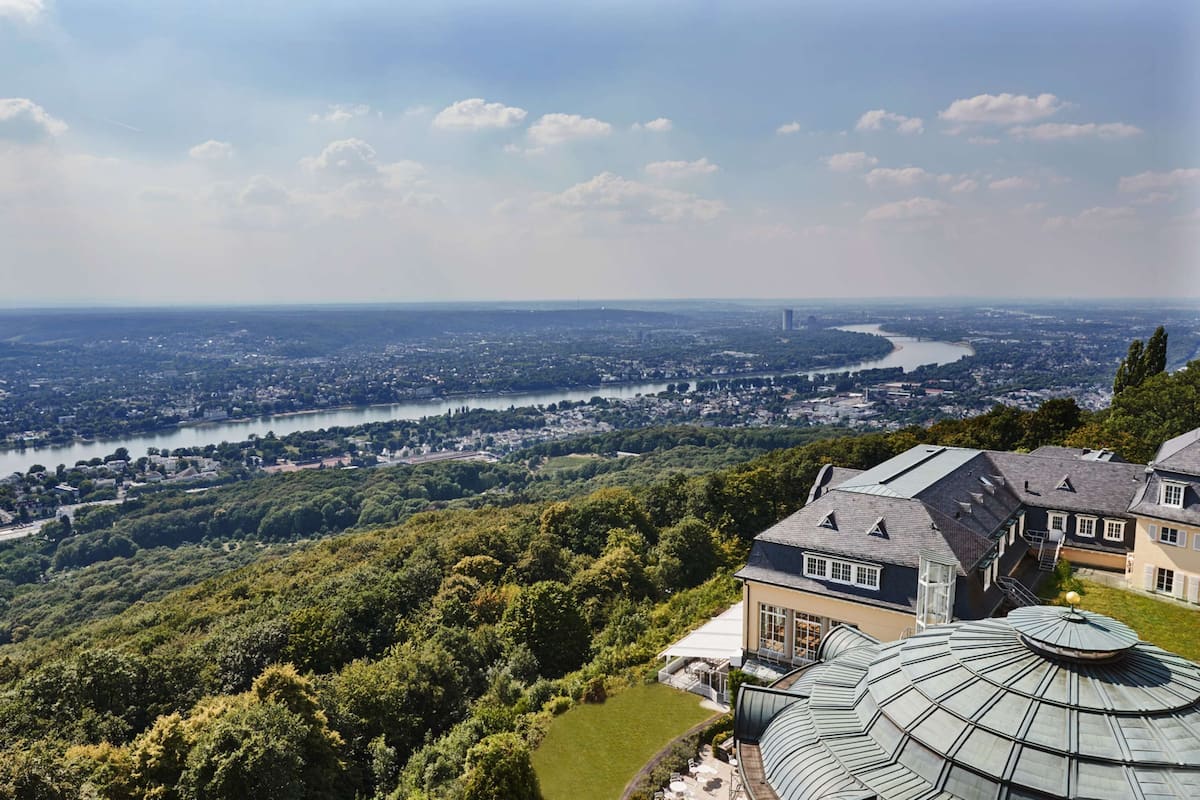 A panoramic view of a cityscape with a river, lush greenery, and a large building with a distinctive dome roof.