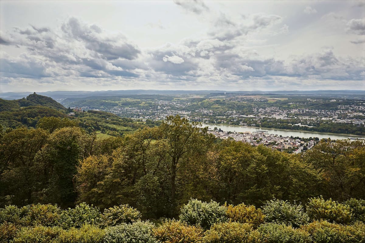 A panoramic view of a town nestled in a valley with a river running through it, surrounded by dense forests and hills.