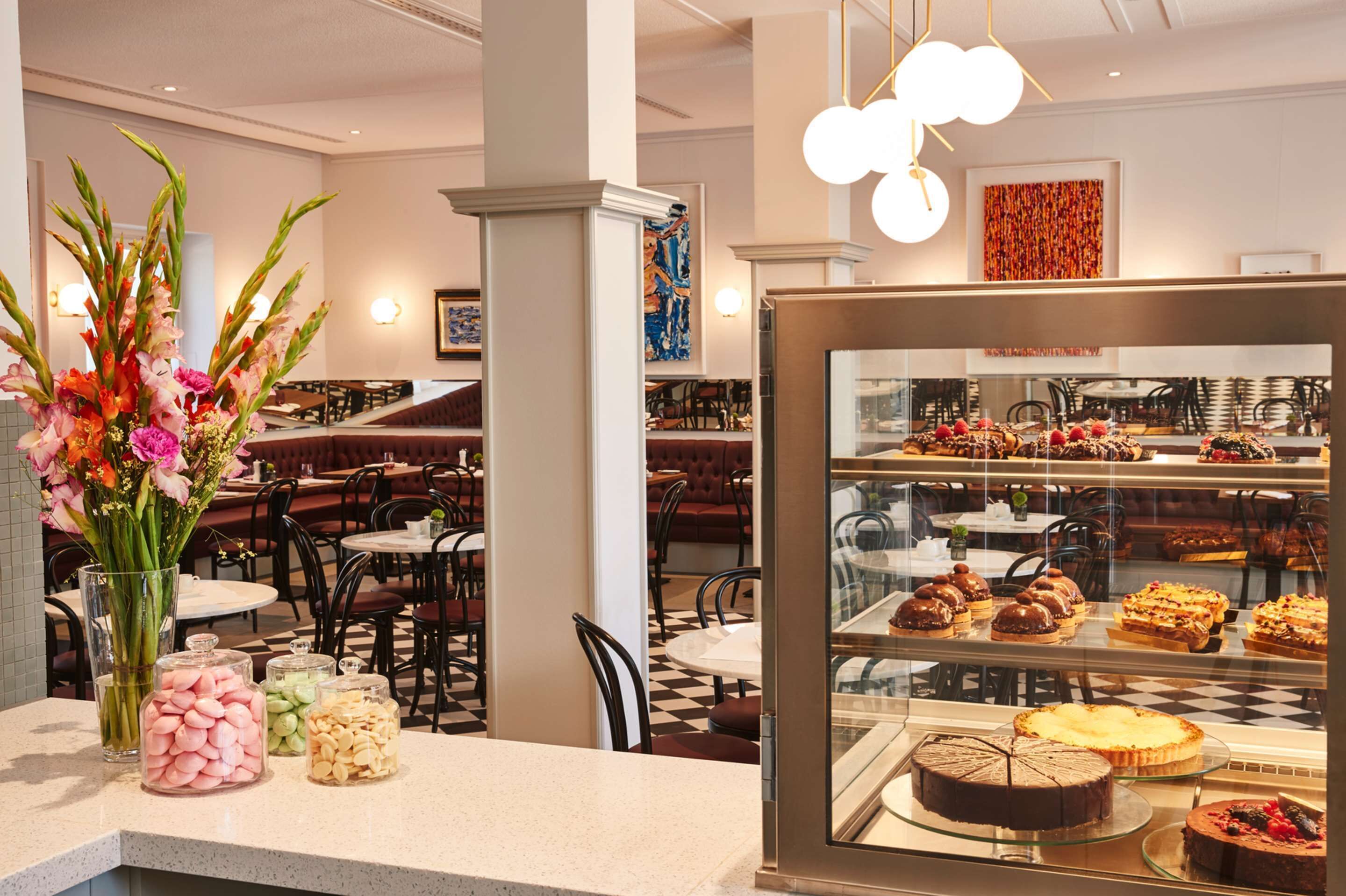 A restaurant with a glass display case of desserts, a vase of flowers, and jars of snacks on the counter.