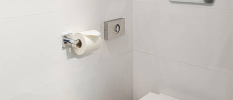 Un baño moderno con un inodoro blanco, un dispensador de papel higiénico y un botón de descarga.