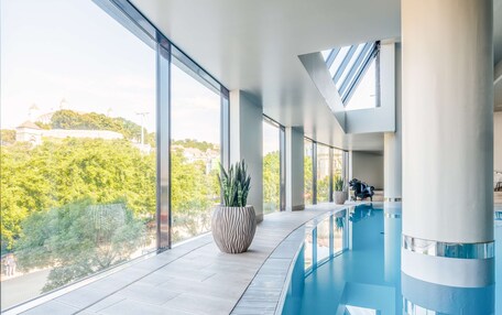 A modern indoor swimming pool with large windows and a view of greenery and buildings.