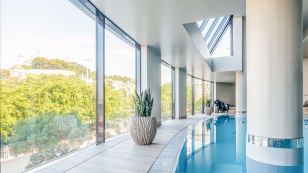 A modern indoor swimming pool with large windows and a view of greenery and buildings. - Park Inn by Radisson Danube Bratislava (Bratislava)