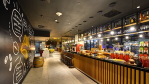 A modern bar area with a counter displaying various food items and a wall with decorative text and drawings. - Park Inn by Radisson Danube Bratislava (Bratislava)