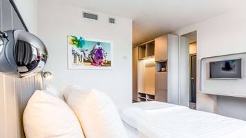 A hotel room with a bed, a large mirror, a picture on the wall, and a TV mounted on the wall.
