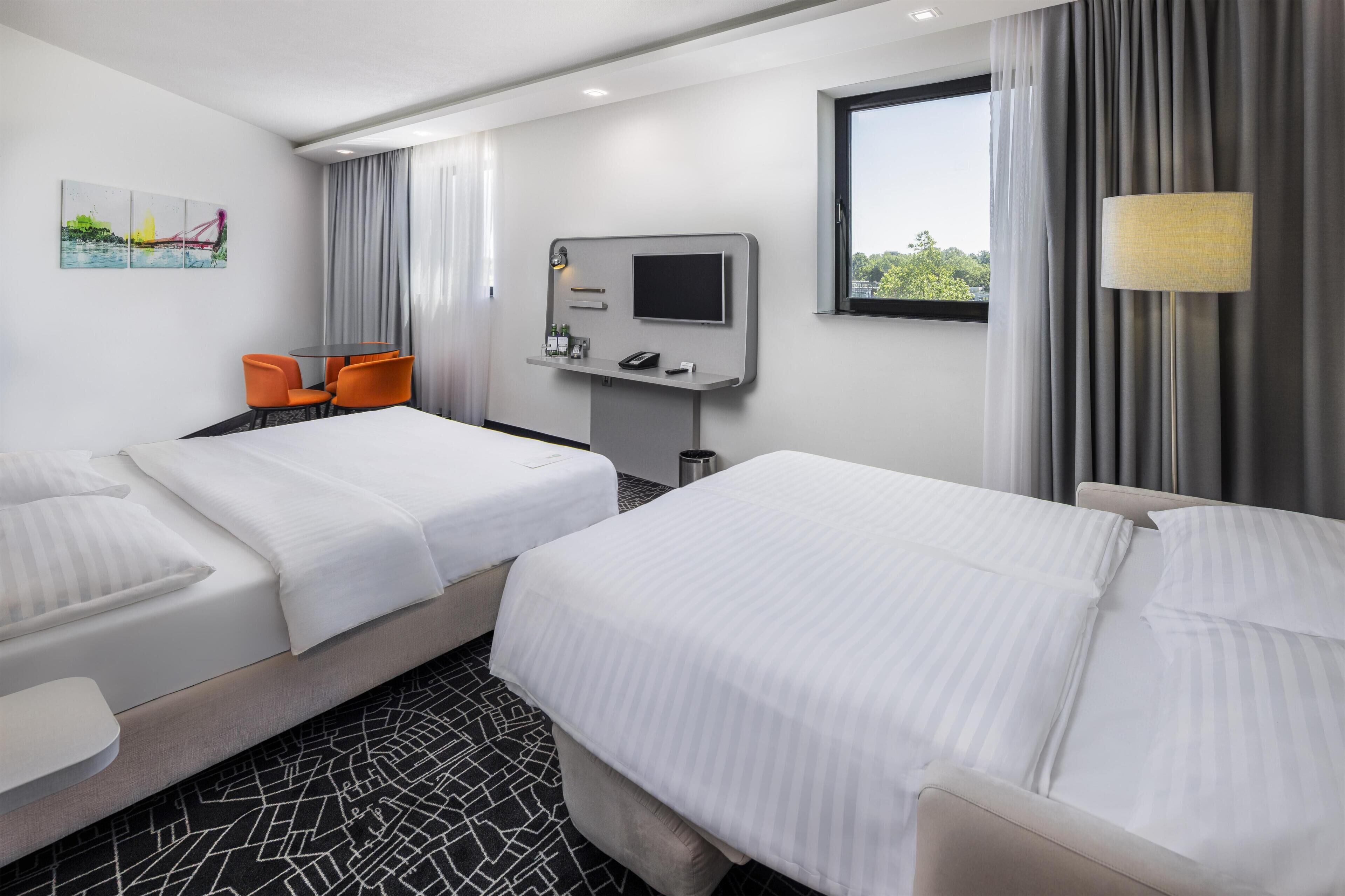 A hotel room with two beds, a desk with a TV, a chair, and a window with curtains.