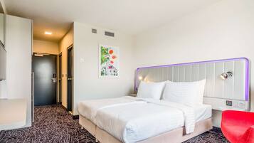 A hotel room with a bed, a red chair, and a door leading to another room.