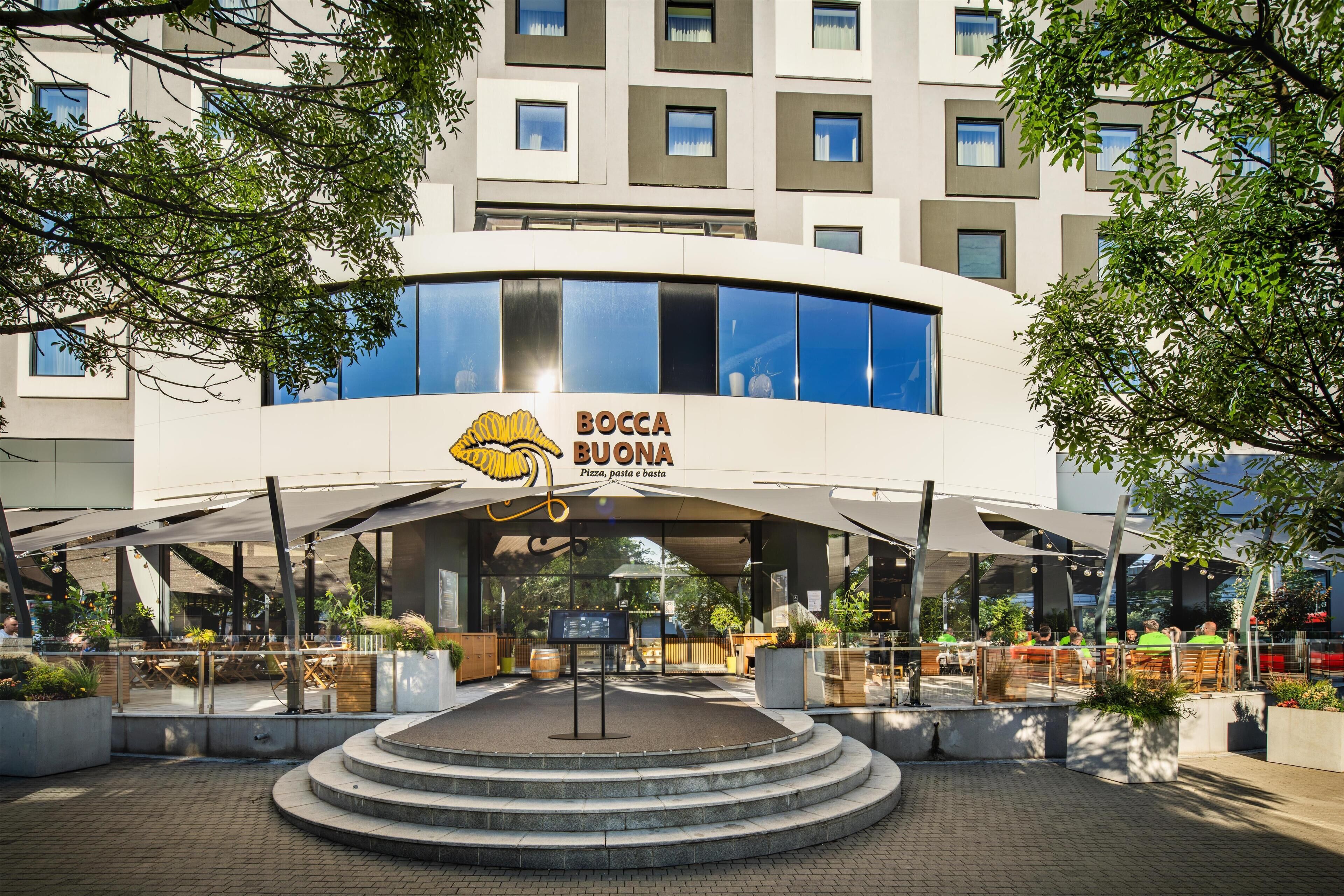 A modern building with a central entrance, a pizza logo, and outdoor seating.