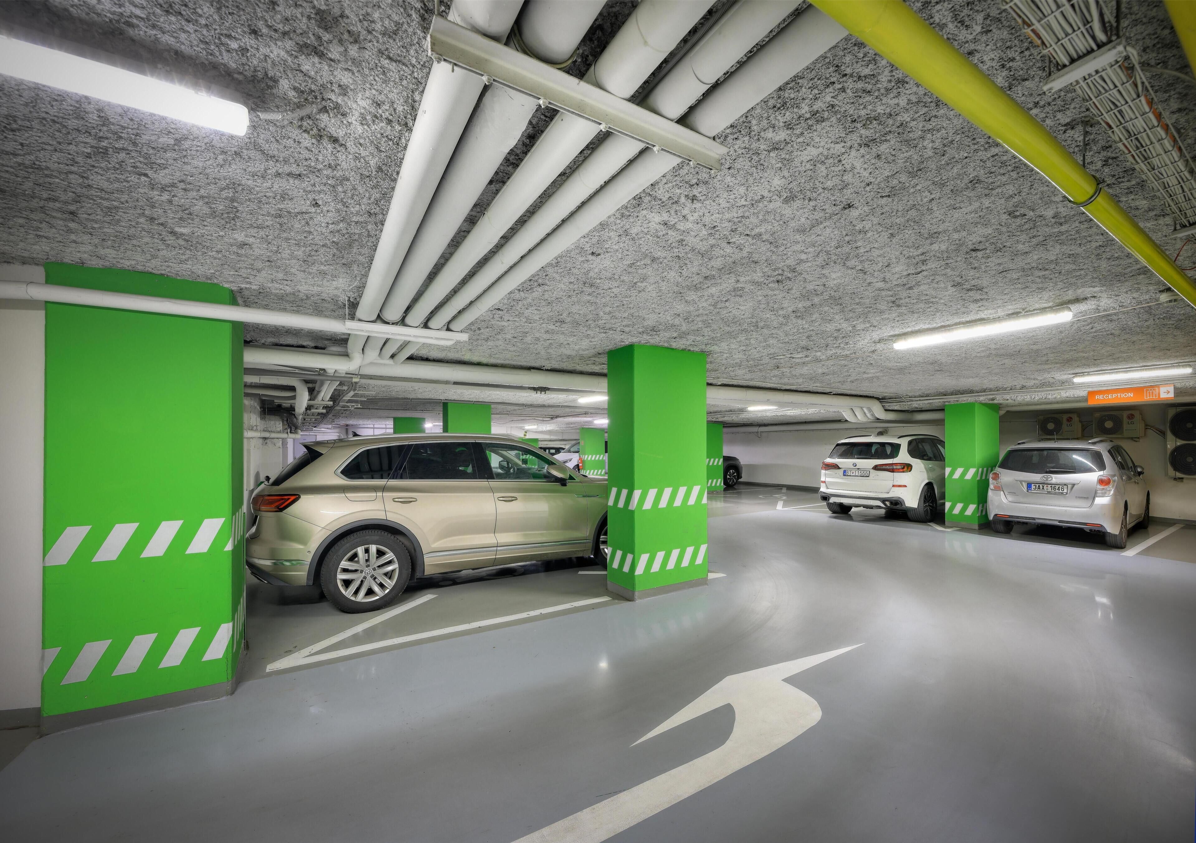 Un parking souterrain avec de nombreuses voitures, des piliers verts et des flèches directionnelles peintes sur le sol.
