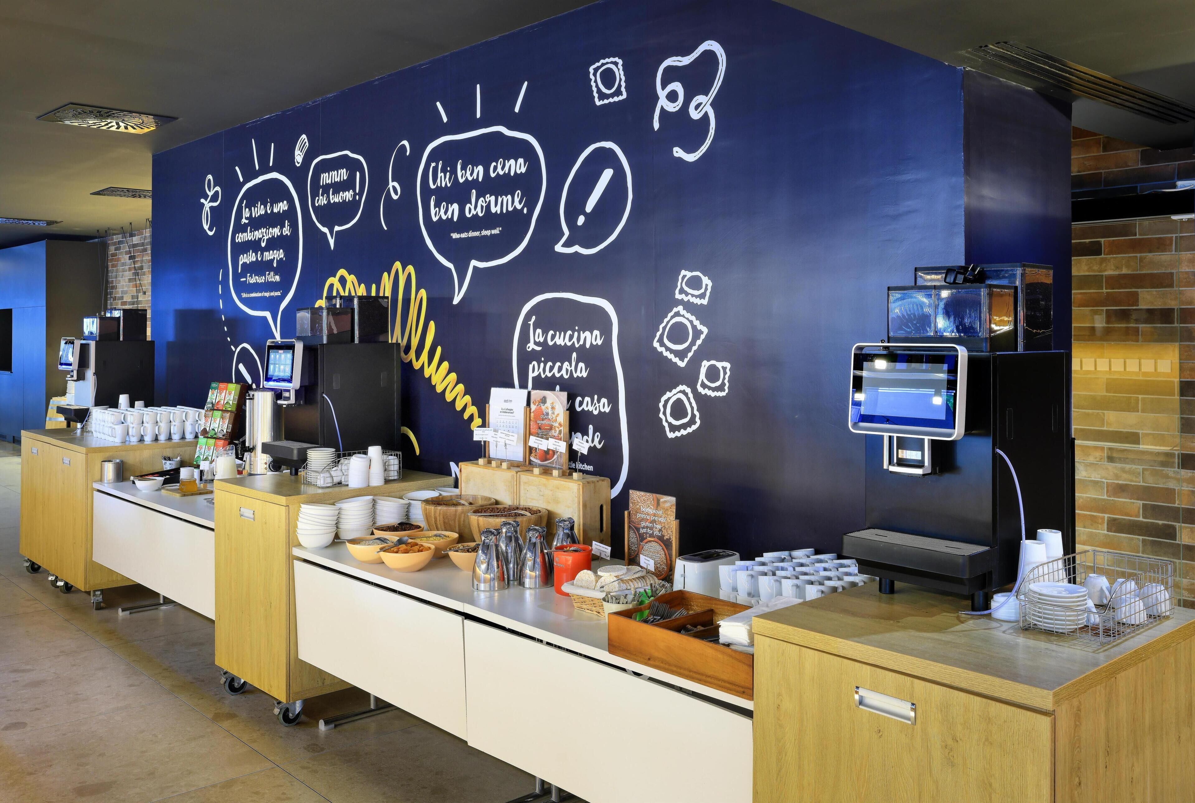 Una barra de desayuno con diversas opciones de alimentos, una máquina de café y una pared con citas inspiradoras.