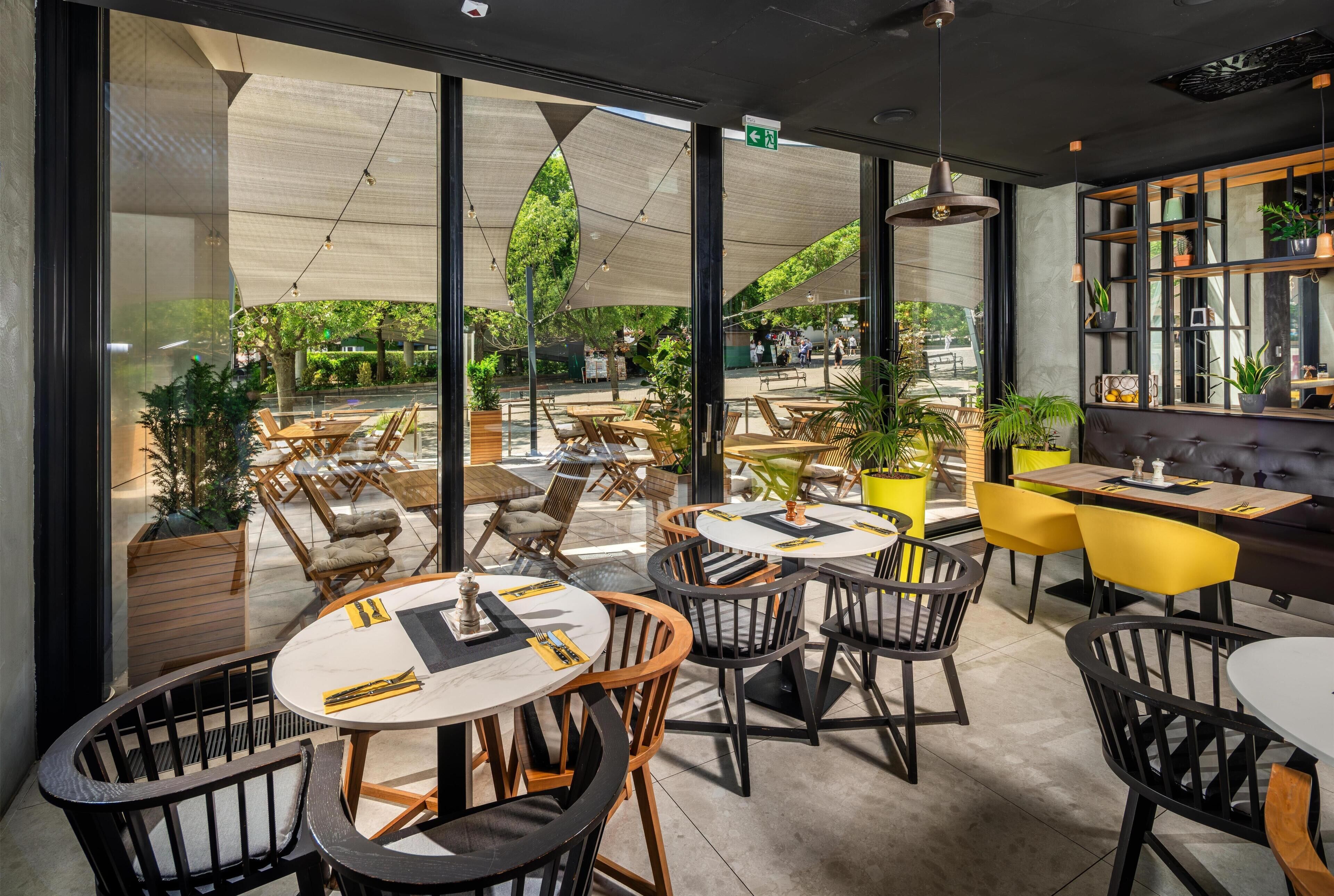 Un espace intérieur aménagé avec des tables et des chaises, de grandes fenêtres et une vue sur la rue.