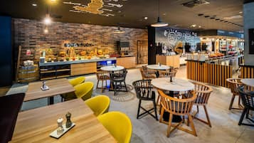 A restaurant interior with a brick wall, wooden tables, yellow chairs, and a bar area.