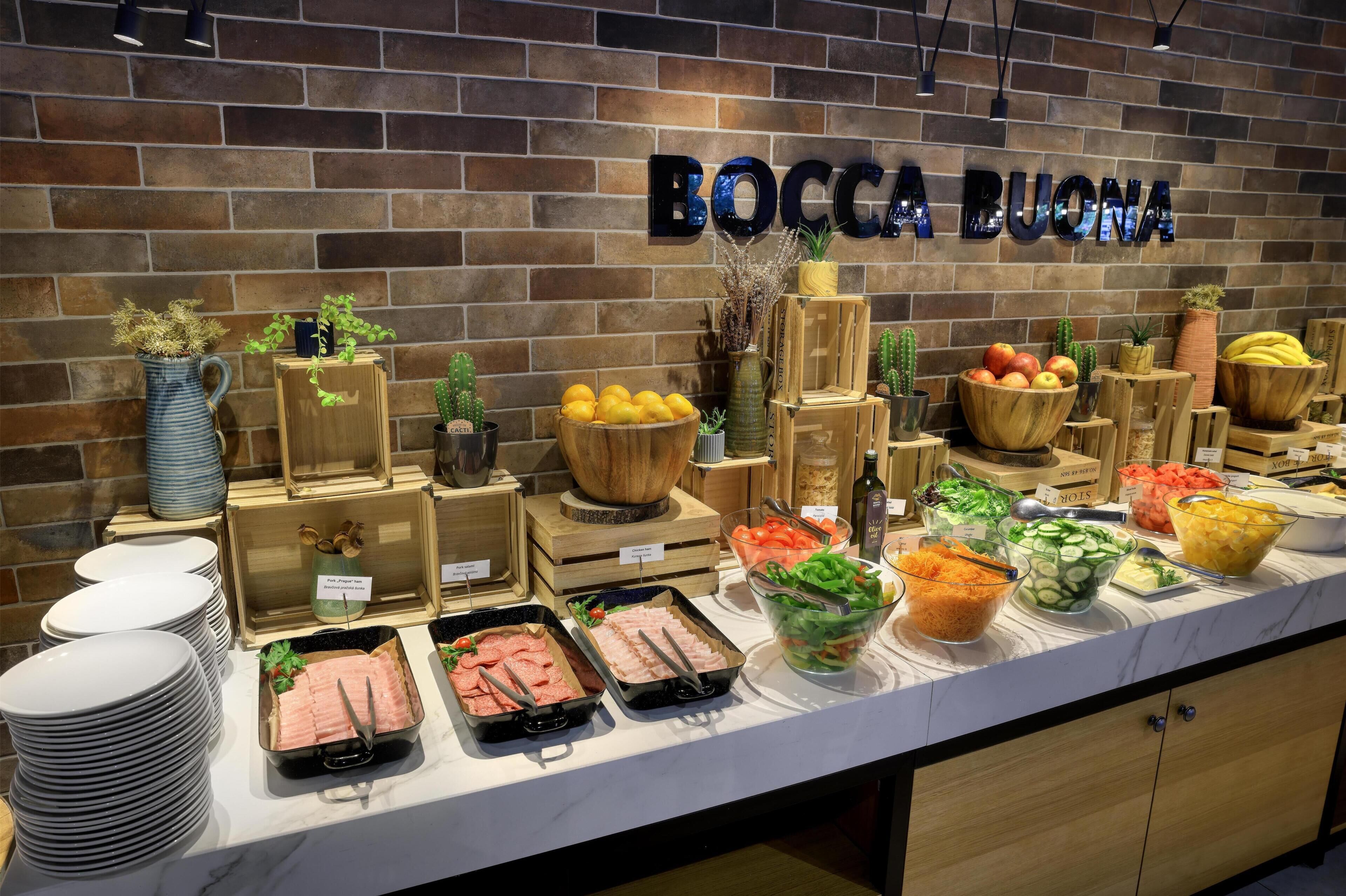 A buffet with various food items and a sign that reads 'BOCCA BUONA' on a brick wall.