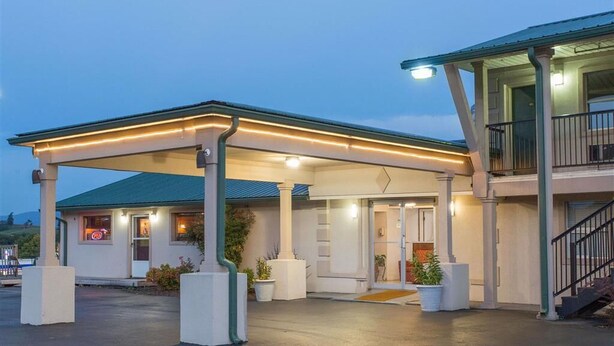 Un motel con área de estacionamiento techada, un edificio de un solo piso y un balcón a la derecha.