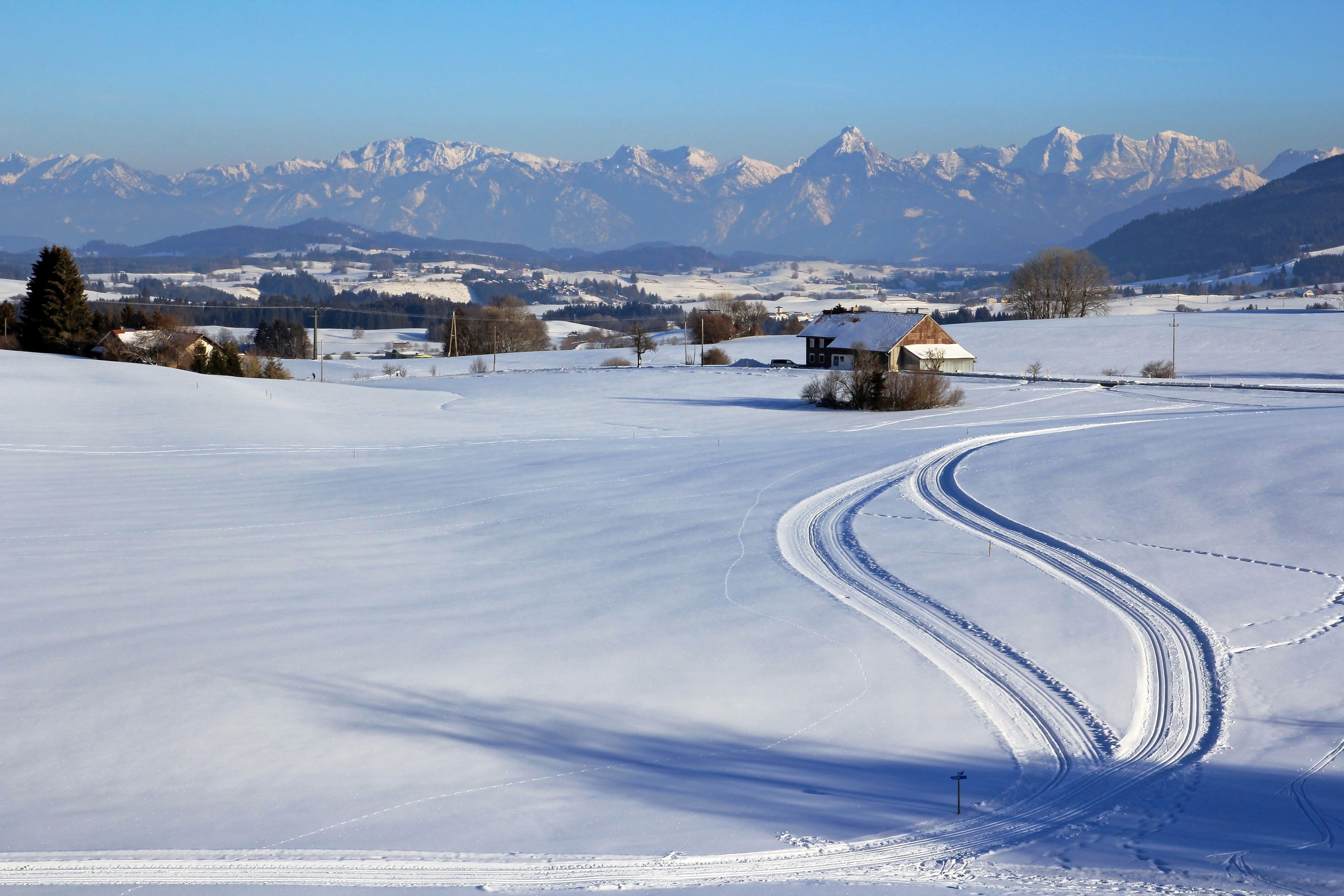 Un paysage enneigé avec une maison et des montagnes en arrière-plan.